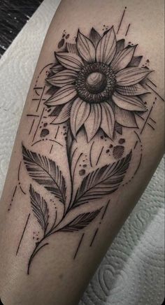 a black and white tattoo with a sunflower on the arm, in front of a woman's leg