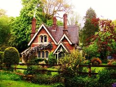 a house in the middle of a lush green field with trees and bushes around it