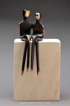 two black and gold figures sitting on top of a white block with their backs to each other