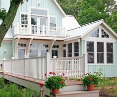 a blue house with white railings and flowers on the front porch, surrounded by greenery