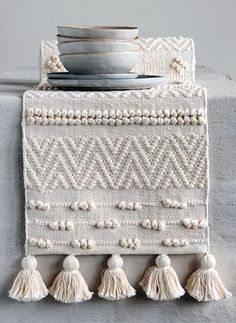 a white table runner with tassels on it and a bowl in the middle