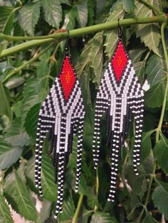 two pairs of black and white beaded earrings hanging from a branch with green leaves in the background