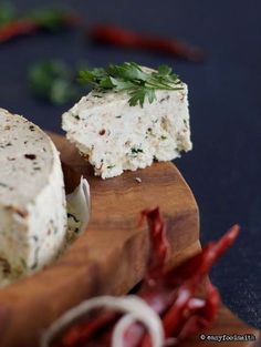 two pieces of cheese sitting on top of a wooden cutting board next to red peppers