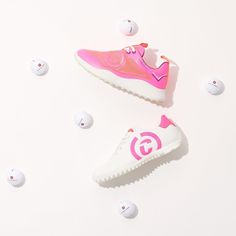 two white and pink tennis shoes surrounded by balls on a white surface with the letter g