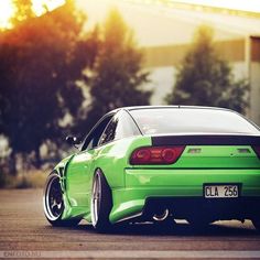 a green car parked in front of a building with the sun shining down on it