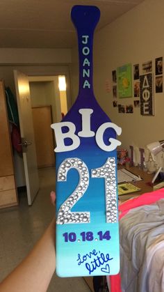 a person holding up a sign that says big 21 in front of a room with pictures on the walls