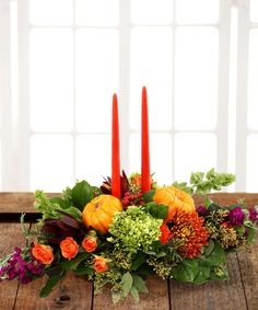 an arrangement of flowers and candles sits on a wooden table in front of a window