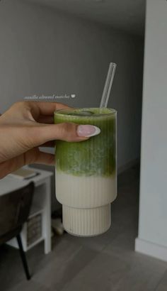 a hand holding a green drink with a straw in it's cup and the bottom half filled with liquid