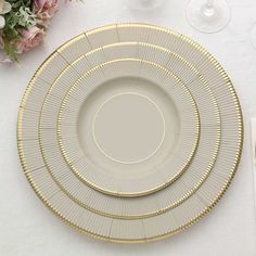 three plates with gold rims are sitting on a table next to wine glasses and flowers