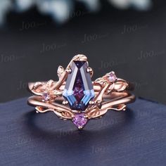 a pink and blue stone ring on top of a black surface with other jewelry items in the background