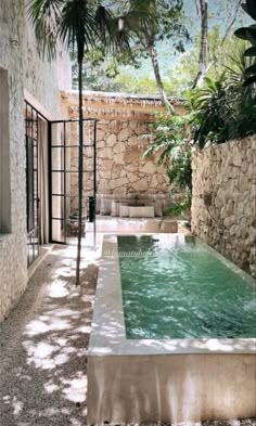 an outdoor hot tub in the middle of a courtyard with stone walls and trees surrounding it