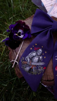 two purple ties with knights on them sitting in the grass next to flowers and brochures