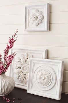 three white frames with pink flowers in them on a table next to a vase and wall hangings