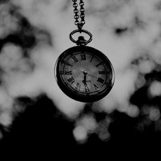 a black and white photo of a pocket watch hanging from a chain with trees in the background