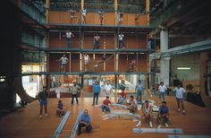 several people are standing and sitting on the floor in an open area with scaffolding