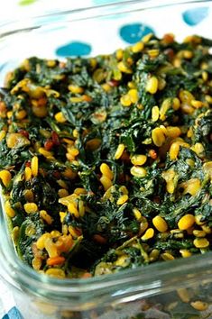 a glass dish filled with corn and spinach on top of a blue polka dot table cloth