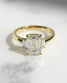 an emerald - cut diamond ring sits on a marble surface