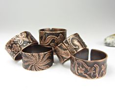 five rings with designs on them sitting next to a rock and some other items in the background