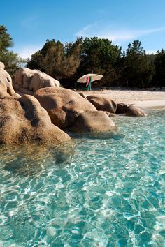 the water is crystal blue and there are rocks in the foreground with an umbrella sticking out of it