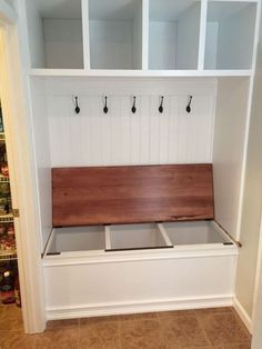 a white bench with wooden seat and hooks on it's back wall in a kitchen