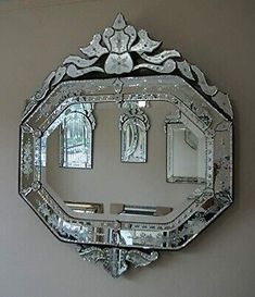 an ornate mirror hanging on the wall above a shelf with two mirrors and a candle holder