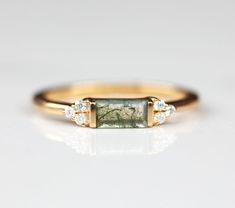 If you are looking for something delicate and simple but still perfect to stack with your other rings, look no further than our Malia ring. With a tapered Moss agate baguette and moissanite, it is the perfect promise ring or as a gift for your loved one. Details: Center stone Gemstone: Moss Agate Stone Shape: Baguette Measurements: approx. 6x3mm Side stones Gemstone: Moissanite Shape: Round Measurements: 1.3mm (6) Band measurements: approx. 1.8mm wide, approx. 1.5mm thick Pictured in vermeil, av Moss Agate Stone, Baguette Engagement Ring, Green Gemstone Ring, Alternative Wedding Rings, Agate Engagement Ring, Moss Agate Ring, Baguette Ring, Lace Bands, Agate Ring