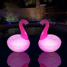 two pink flamingos sitting on top of a pool next to each other at night