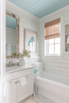 a white bathroom with blue ceiling and wooden window shades on the windowsill, along with a bathtub