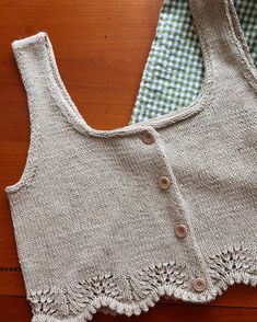 two knitted vests sitting next to each other on a wooden table with buttons