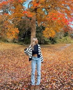 a woman standing in front of a tree with fall leaves on the ground around her