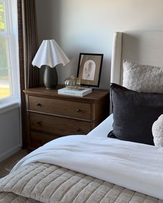 a white teddy bear sitting on top of a bed next to a night stand and lamp