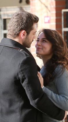 a man and woman standing next to each other in front of a red brick building