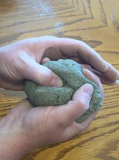 a person holding a piece of green clay in their hands on a wooden table top