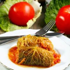 two stuffed cabbages on a white plate with fork and knife next to some lettuce