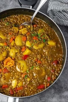 a pot filled with lentils and potatoes on top of a table next to a spoon