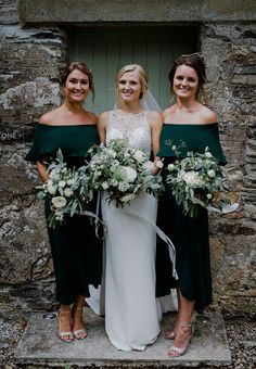 three bridesmaids standing in front of an old stone building with their bouquets