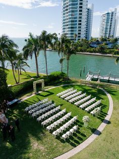 an outdoor ceremony setup with white chairs and palm trees by the water in front of high rise buildings