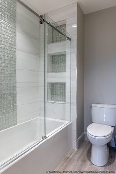 a white toilet sitting next to a bath tub in a bathroom under a glass shower door