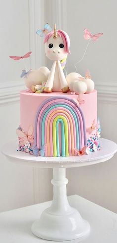 there is a pink cake with a unicorn on top and rainbows in the background