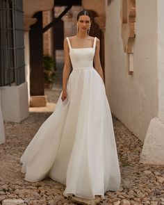 a woman in a white wedding dress walking down a cobblestone street with her hand on her hip