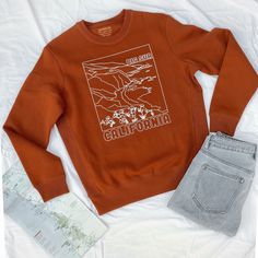 Hand drawn from one of our favorite and most well known Big Sur coastal spots. With California wildflower poppies. Perfect gift for any outdoorsy, coast lover or Californian. The perfect everyday sweatshirt to match everything! Made with responsibly California grown Supima organic cotton with the highest sustainable and ethical standards where workers are paid fairly. This garment is produced in a wind mill powered, Fair Trade Certified™ facility. This means that our products were grown, harvest Casual Sweatshirt With Screen Print For Outdoor Activities, Vintage Fall Tops For Outdoor, Vintage Tops For Fall Outdoor, Vintage Fall Outdoor Tops, Brown Relaxed Fit Top For Outdoor, Casual Orange Top For Outdoor, Brown Crew Neck Top For Outdoor, Casual Cotton Sweatshirt For Adventure, Retro Crew Neck Tops For Outdoor Activities