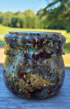 a glass jar sitting on top of a wooden table next to a forest filled with trees