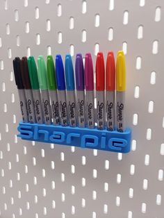 six pens are lined up in a holder on a white wall with holes for writing