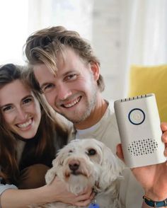 a man and woman holding a dog with a remote control in front of their face