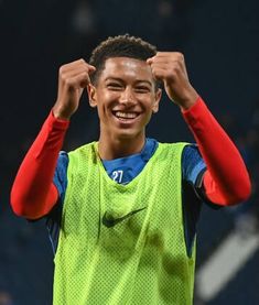 a young man is smiling and holding his hands up in the air while wearing a green shirt