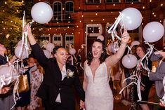 a bride and groom are holding balloons in the air as they walk down the aisle