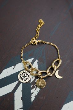 This simple yet elegant gold tone chain bracelet with 3 charms that depict a round star, round WAR emblem and a moon that dangle from the center, boasts a unique design. Perfect for casual wear or those extra special occasions. Support at-risk women when you purchase these gorgeous handmade bracelets. Dimensions: 6" long with 2" extender. Strawberry Lip Balm, Round Star, Vanilla Lip Balm, Swirl Soap, Gold Bubbles, Gold Chain Bracelet, Onyx Bracelet, Brass Necklace, Gold Bracelet Chain