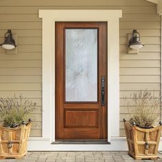 two planters with plants in front of a door on the side of a house