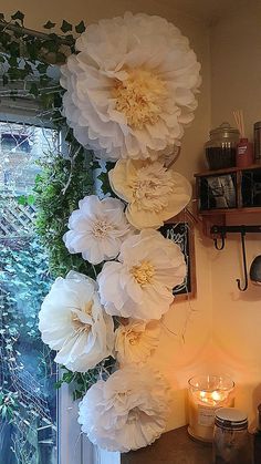 white flowers are hanging on the wall next to a candle