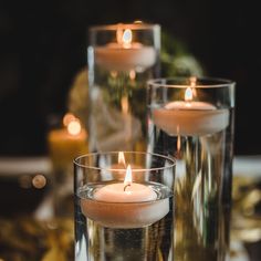 three lit candles sitting on top of a table next to glass vases filled with water